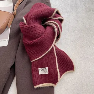 Détail d'une écharpe en maille bordeaux avec bordure blanche et étiquette tissée