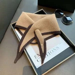 Detail of camel knit triangle scarf with dark brown trim and a small metal charm