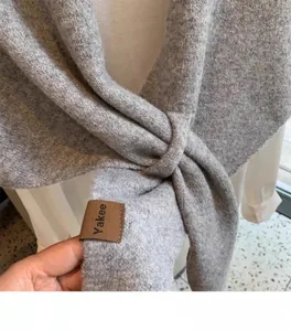 Detail of grey wool blend knit shawl with texture and branded leather tag on white shirt