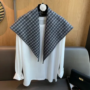 Detail view of a thick grey plaid triangle scarf paired with a white shirt on a hanger