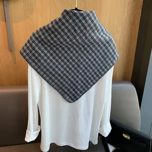Detail of grey plaid woven triangle scarf styled over a white casual long sleeve cotton shirt