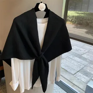 Detailed close-up of a black wool blend knitted shawl with elegant front cross-tie knot