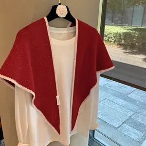Detalle de chal de lana roja con bordes de ganchillo crema y etiqueta de material 100% lana