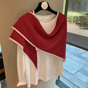 Detalle del chal de lana roja con borde ondulado blanco sobre un tejido de alta calidad