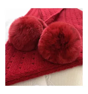 Detailed macro view of red hollow knit triangle scarf with fluffy faux fur pom-poms