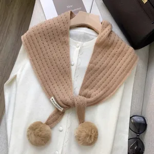 Detail of wool cashmere triangle scarf showing camel knit texture and pompom accents