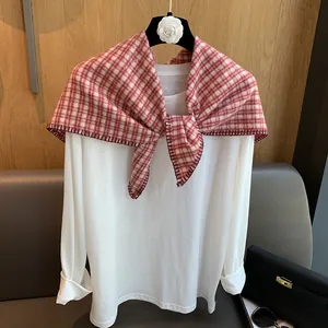 Detail of red and white checkered knitted triangle scarf styled on white long sleeve top