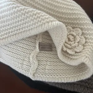 Detail showing the 100% wool knit texture and hand-crocheted flower on the cream beanie