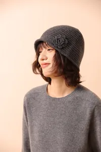 Detail of dark grey knit cloche hat with crochet flower accent on a minimalist background