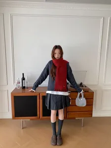 Full view of model wearing a red wool blend fringe scarf with a gray knit sweater