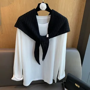 Détail du châle en laine noire à rayures ajourées sur un t-shirt blanc à manches longues