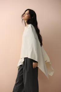 Detailed view of cream knitted poncho featuring asymmetric cut and premium wool blend fabric
