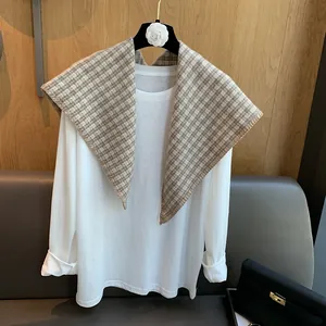 Detail of checkered knit shawl layered over a plain white long sleeve shirt on a hanger