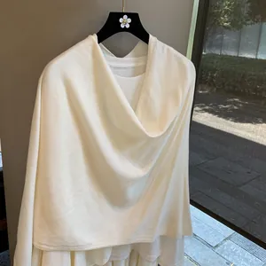 Elegant white knitted shawl cape for women with asymmetrical drape on a hanger