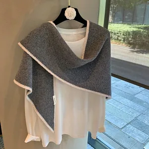 Detalle de chal de lana gris con bordes de punto blanco y etiqueta de 100% pura lana