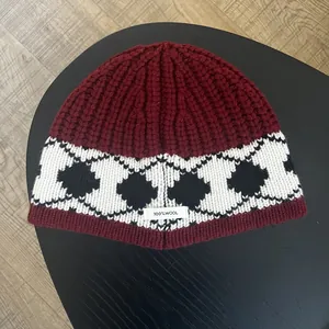 Close-up of 100% wool label on thick burgundy and black diamond knit beanie hat