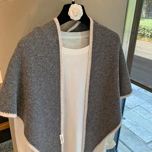 Detalle de un chal de lana gris con textura de canalé vertical y etiqueta de marca tejida