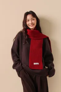 Close-up of a red chunky knit wool scarf with a white logo tag on a brown sweater