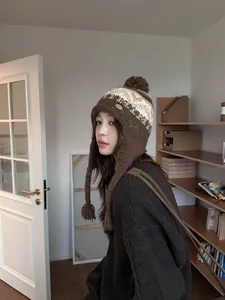 Détail de la chapka en tricot marron foncé avec cache-oreilles et pompon décoratif