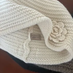 Close-up of a white wool knitted beanie with 100% wool label and crochet flower detail