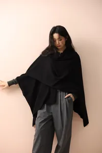 Detail view of the soft black knit poncho with elegant asymmetrical drape and texture