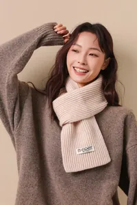 Detail of cream rib-knit wool scarf showing texture and brand label on a model