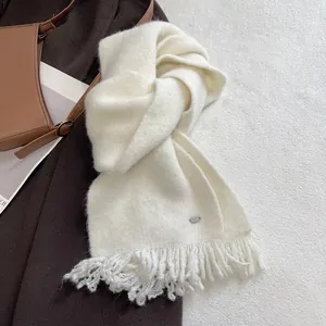 Detail of soft cream wool blend knit scarf with fringe and silver metal logo tag