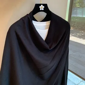 Detail of elegant black knitted poncho shawl showing V-neck layering over a white shirt