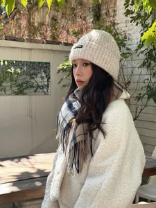 Close-up of beige knit beanie with Keep Going label and wool plaid tassel scarf