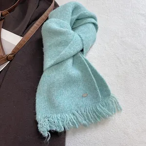 Detail of mint green knit scarf featuring soft tassel trim and a small metal logo plaque