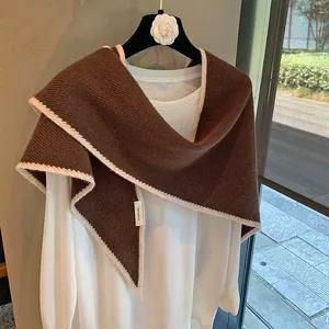 Detalle de chal de lana marrón con costuras onduladas blancas y etiqueta de composición