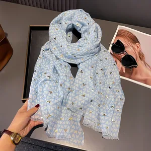 Close-up of light blue scarf with gold foil hearts and tassel edge on a black tray