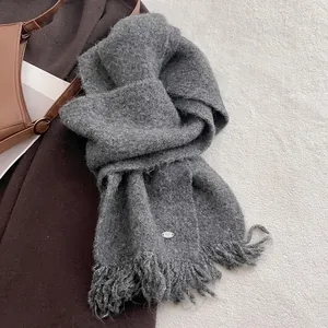 Detailed shot of grey knit scarf showing soft wool texture, fringe, and metal logo tag
