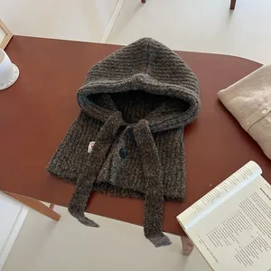 Detail of dark brown chunky knit balaclava with two black buttons on a wooden table