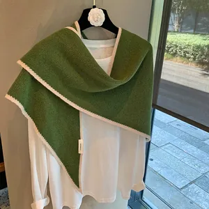 Detalle de chal tejido en 100% lana verde con bordes de ganchillo beige y etiqueta de tela