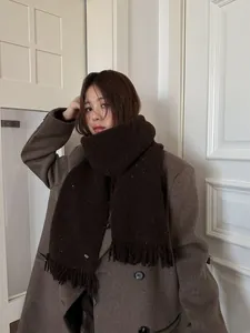 Detail of dark brown wool knit scarf with sequin accents and fringe on a model coat