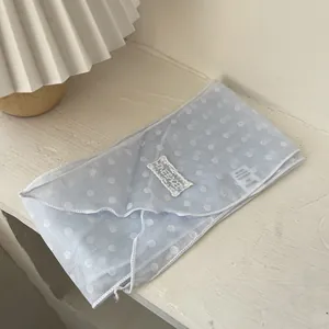 Detail eines hellblauen gepunkteten Halstuchs mit Spitzen-Logo-Patch auf Holzgrund