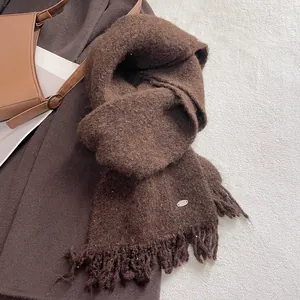 Detail of dark brown wool knit scarf showing fringe edges and metallic logo plaque