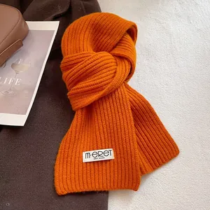 Detail of bright orange knitted wool scarf with vertical ribs and a white brand label