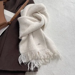 Detail of cream knit scarf with shiny sequins and metal brand logo tag in macro view