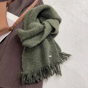 Detail of dark green knit scarf with sequins, fringe edges, and small metal logo