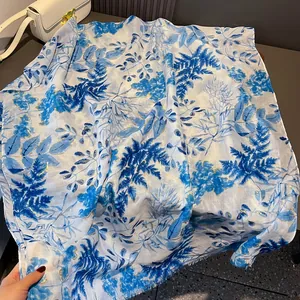 Detailed view of white cotton scarf with blue tropical floral print and gold thread fringe