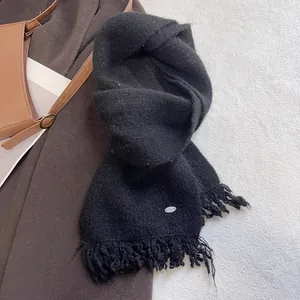 Detail of black knitted scarf with fringe and subtle sequins on white textured rug