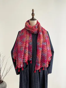Dettaglio di sciarpa bohémien con motivi zigzag colorati e nappine con frange rosse