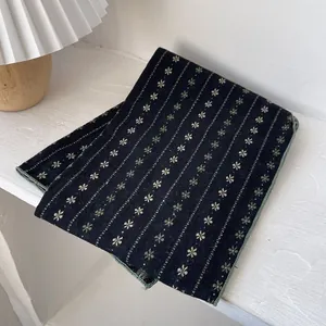 Detail of folded cotton floral scarf with delicate stripe patterns and green border edge