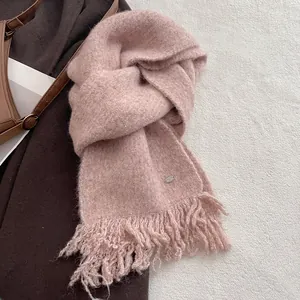 Close-up of pink wool blend knit scarf featuring fringe tassels and a silver logo tag