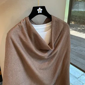 Detail of soft brown knitted poncho shawl draped over white tee showing fabric texture