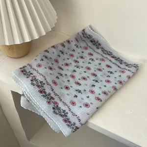 Macro view of pleated floral chiffon scarf with delicate light blue and pink floral patterns