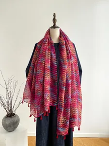 Dettaglio di sciarpa con motivo zigzag colorato e nappine rosse su un manichino