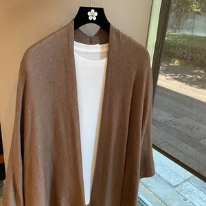 Detail of dark brown knit cardigan with soft texture hanging on a hanger by the window
